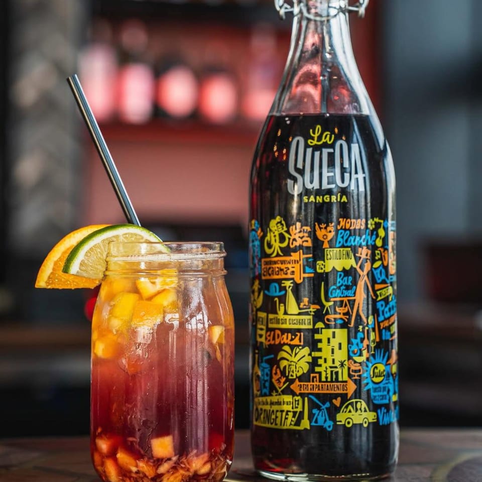A glass of sangria with fruit and a bottle of La Sueca Sangria on a wooden table.