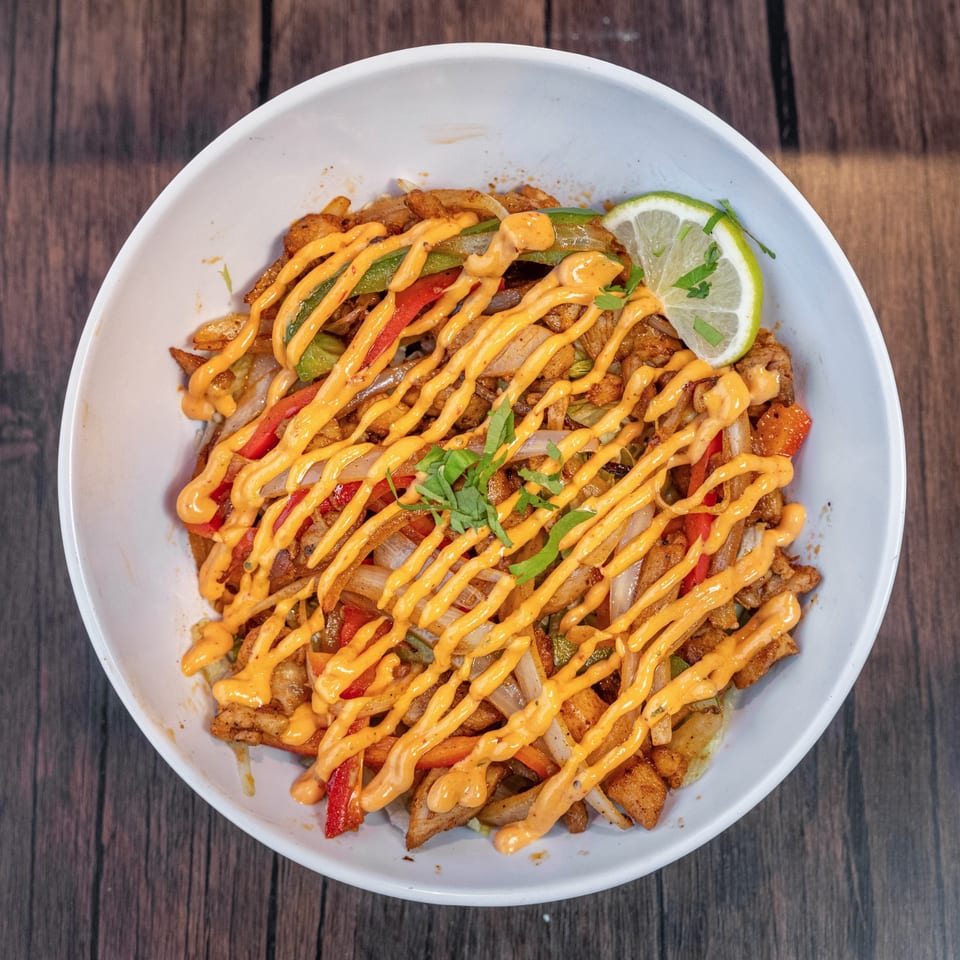 World Taco Factory's chicken fajita bowl with peppers, onions, sauce, and a lime wedge.
