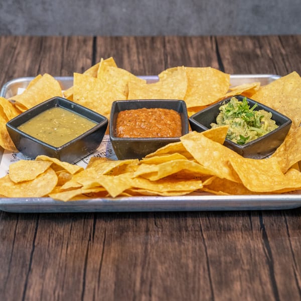 A tray of World Taco Factory tortilla chips with three bowls of salsa, including guacamole.