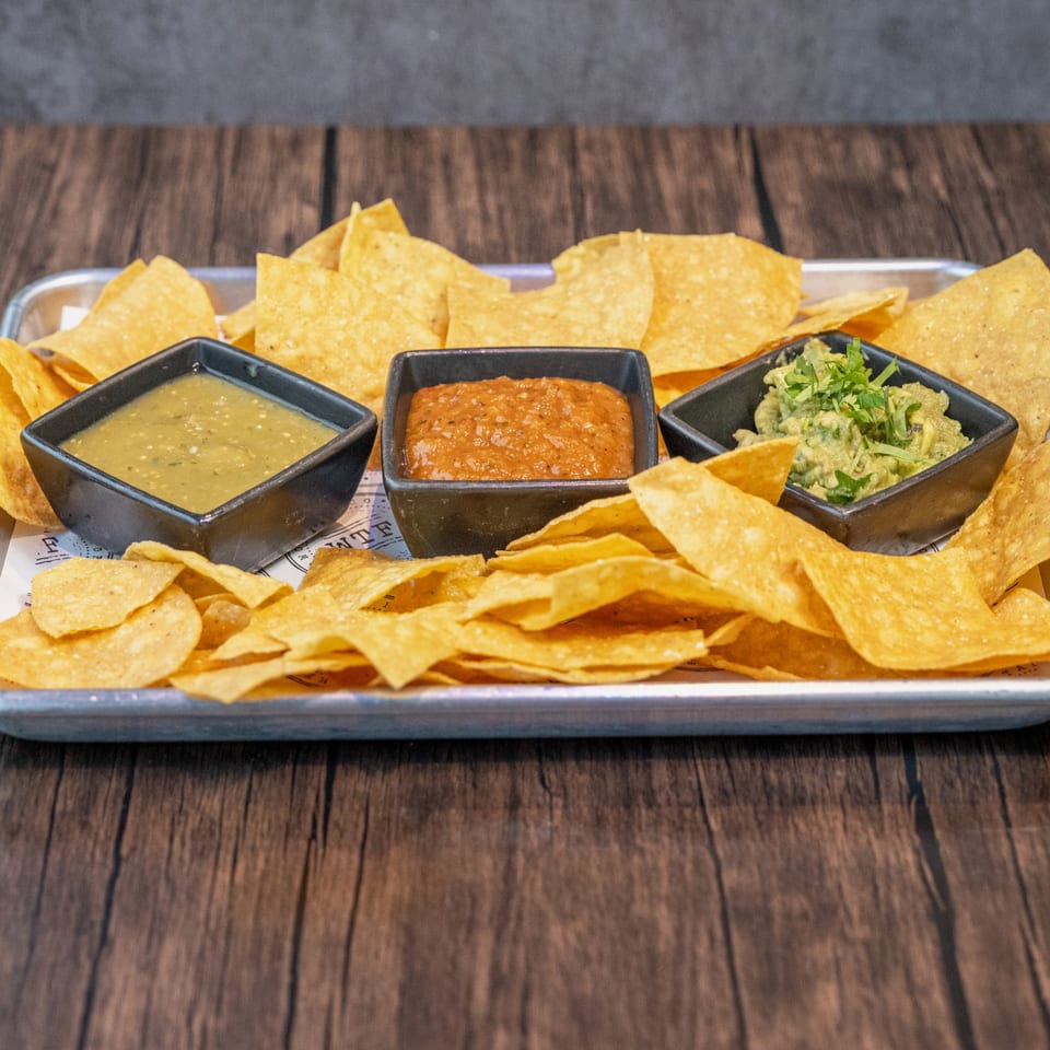 A tray of World Taco Factory tortilla chips with three bowls of salsa, including guacamole.