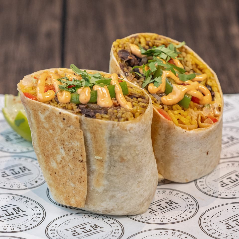 Two World Taco Factory burritos, filled with rice, beans, and vegetables, drizzled with sauce and cilantro.