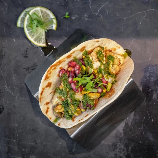 World Taco Factory's taco with cauliflower, pomegranate, and green sauce, served with lime wedges.
