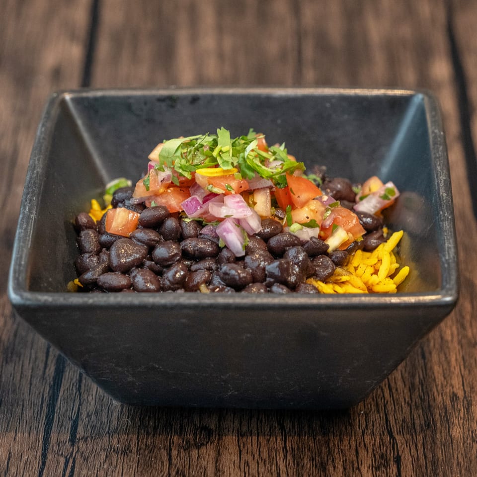 Black beans, yellow rice, pico de gallo, and cilantro in a black bowl on a wooden table.