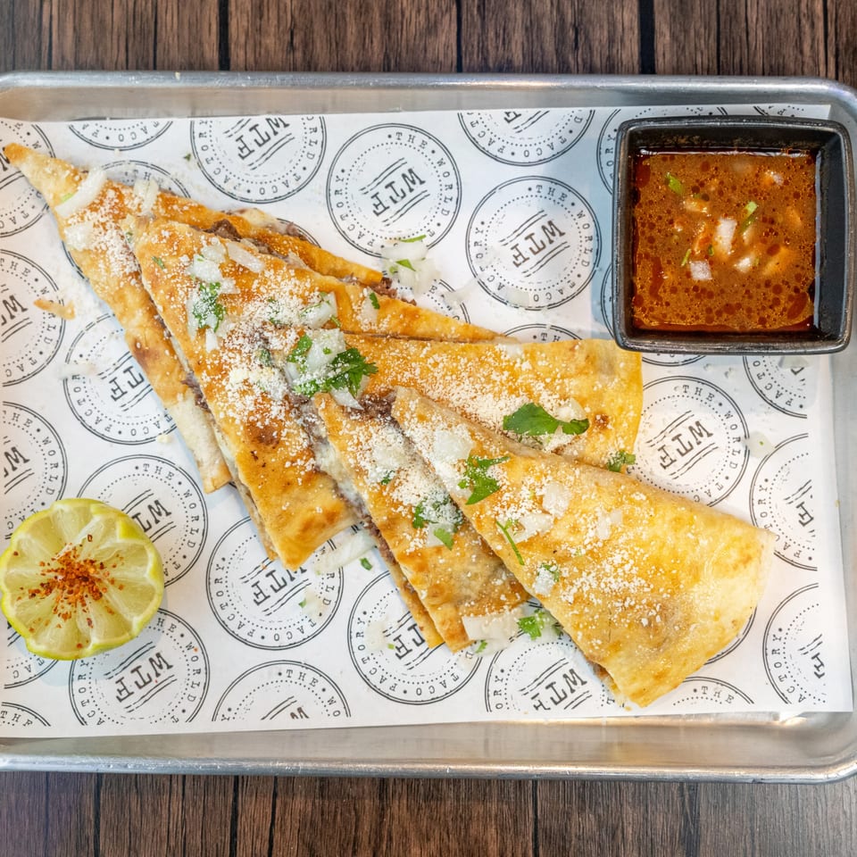 Crispy World Taco Factory birria tacos with consommé and a lime wedge on a metal tray.