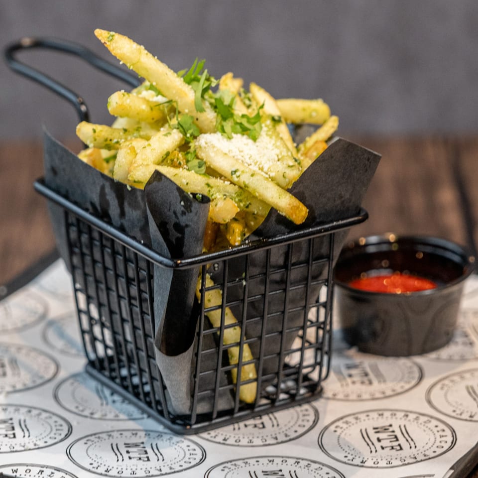 World Taco Factory's crispy fries, seasoned with herbs and cheese, served in a black basket with ketchup.